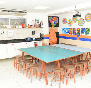 Sala de artes com mesa azul grande e banquinhos de madeira