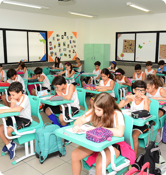 Várias crianças sentadas em carteiras verdes em uma sala de aula, fazendo atividades escolares