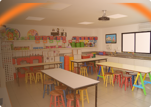 Sala de atividades do Ensino Fundamental do Colégio São Paulo com bancos e mesas coloridas e prateleiras com potes e materiais escolares