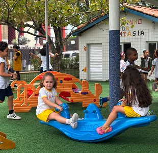Crianças brincando em playground externo com brinquedo azul e laranja