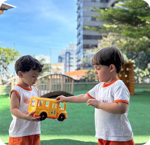 Duas crianças brincando com um ônibus de brinquedo amarelo no gramado