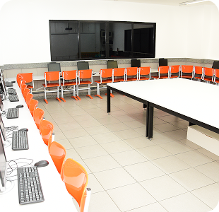 Sala de reunião com cadeiras laranjas em U voltadas para tela