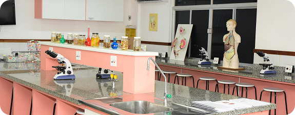Laboratório de ciências com bancada rosa/pêssego, microscópios e boneco anatômico
